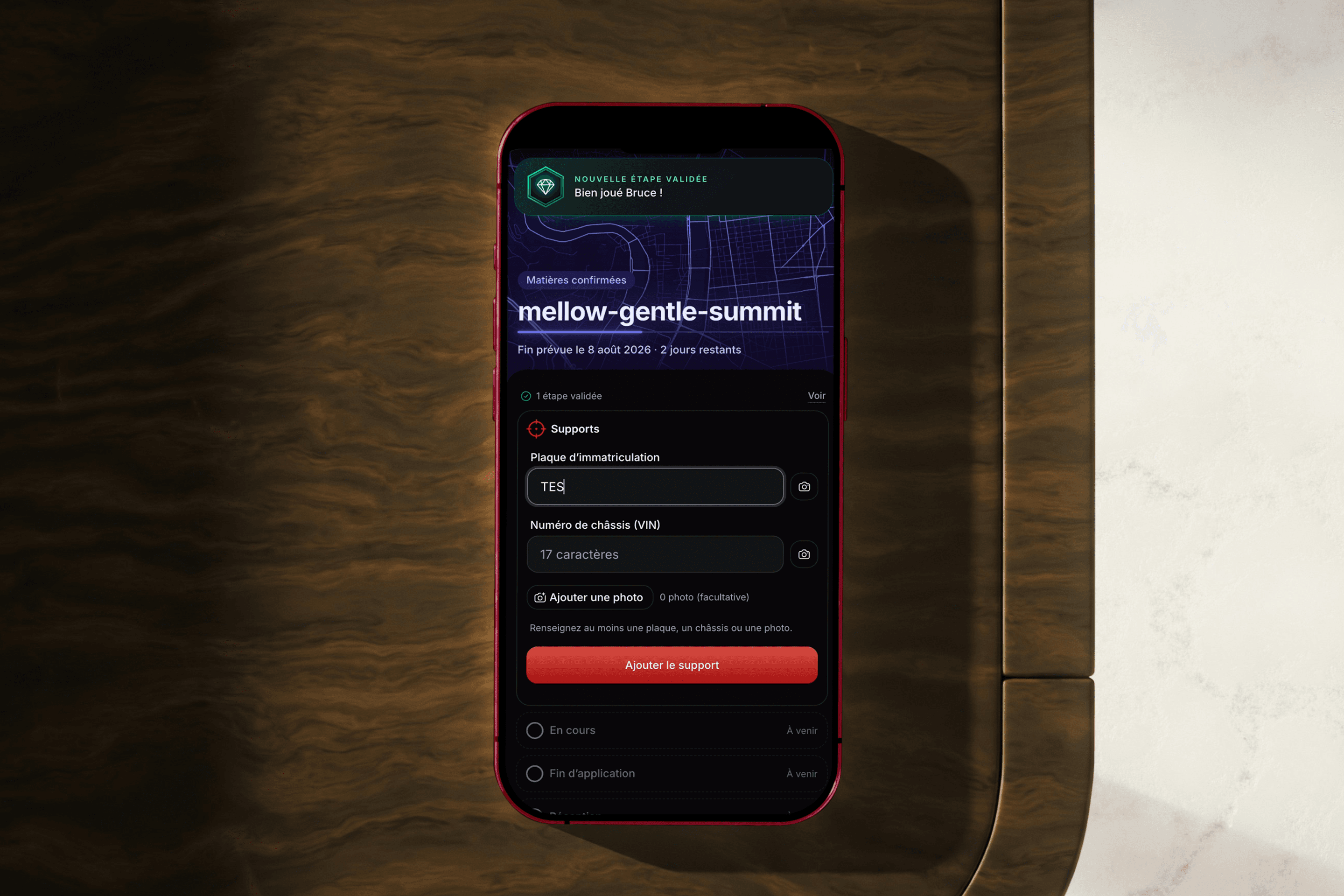 La saisie d'un support — plaque d'immatriculation et numéro de châssis — sur un iPhone posé sur un bureau